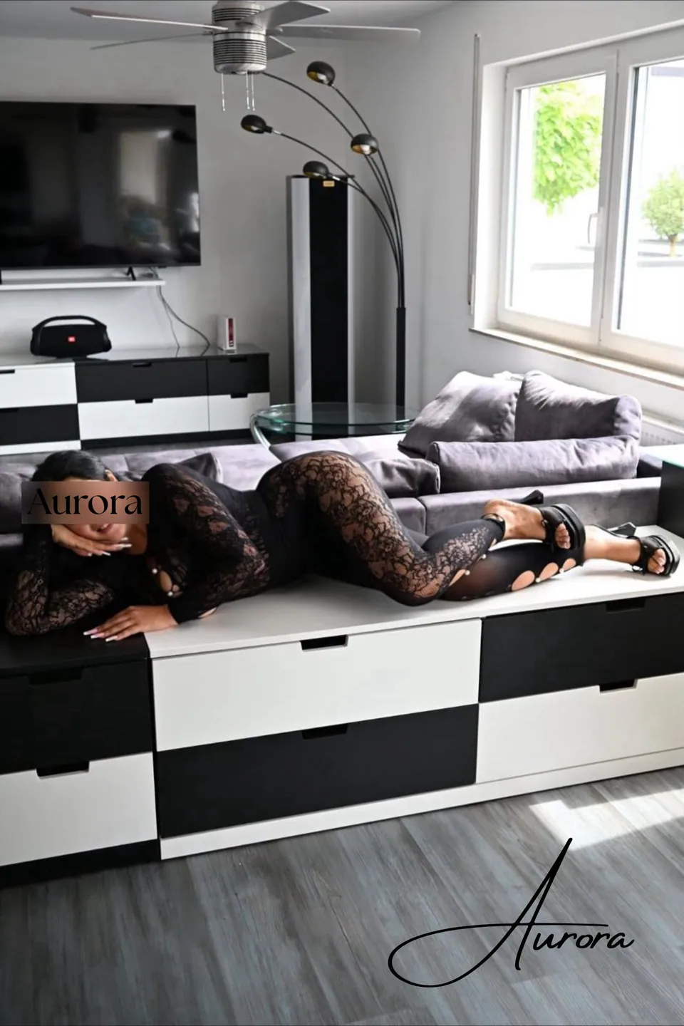 Aurora im schwarzen Spitzen-Catsuit auf einem weißen Sideboard liegend