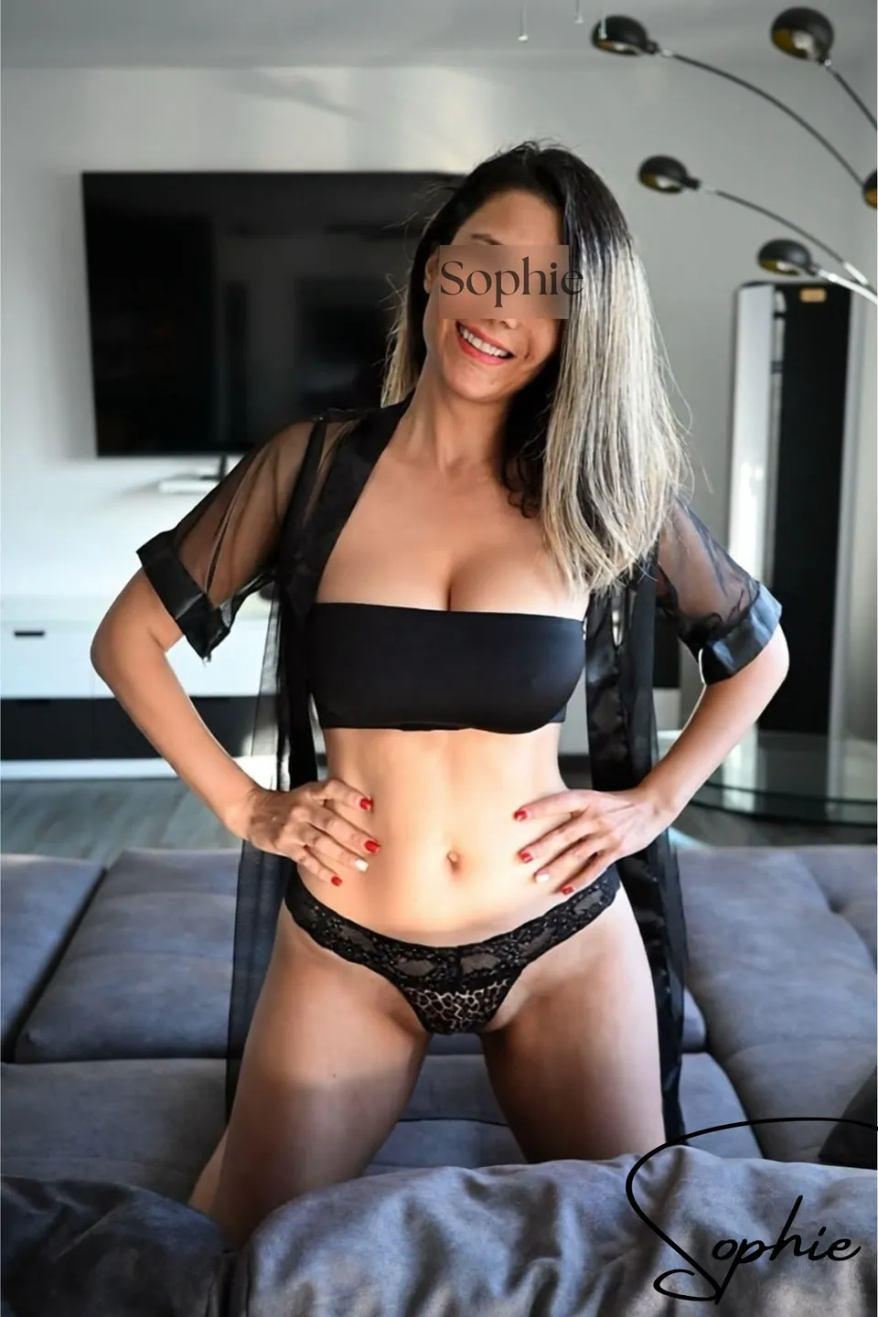 Sophie in schwarzem Bandeau-Top, Spitzenslip und transparentem Kimono auf dem Sofa kniend