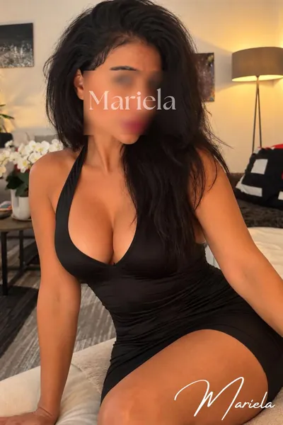 Mariela mit langen dunklen Haaren im schwarzen Neckholder-Kleid auf einem weißen Polster