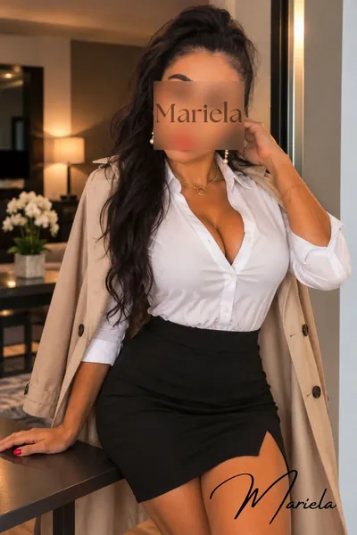 Mariela mit langen dunklen Haaren in weißer Bluse und schwarzem Rock, den Trenchcoat über den Schultern