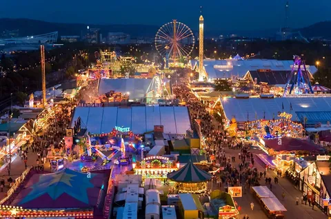 Luftaufnahme des Cannstatter Volksfests am Abend mit Riesenrad und beleuchteten Festzelten
