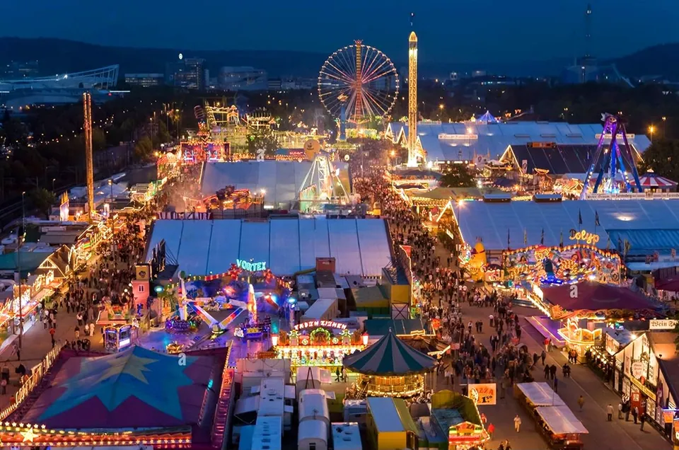Luftaufnahme des Cannstatter Volksfests am Abend mit Riesenrad und beleuchteten Festzelten
