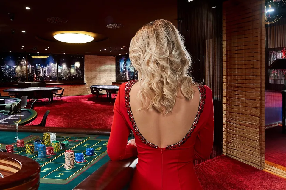 Eine blonde Frau im rückenfreien roten Kleid von hinten am Roulettetisch eines Casinos