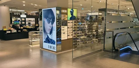 Dior-Verkaufsfläche mit Sonnenbrillen und Werbeplakaten neben einer Rolltreppe