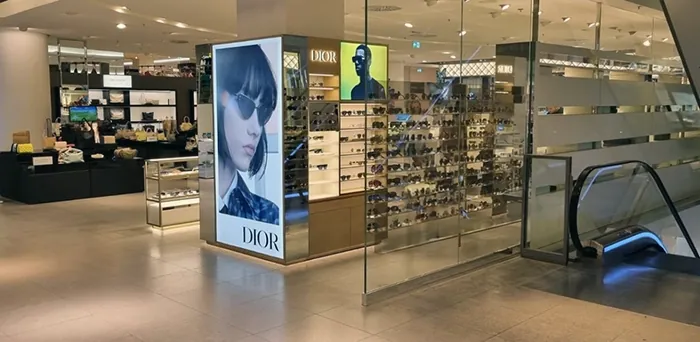 Dior-Verkaufsfläche mit Sonnenbrillen und Werbeplakaten neben einer Rolltreppe