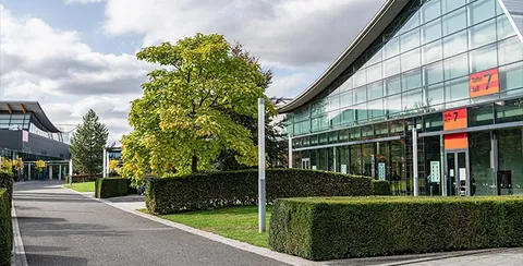 Außenansicht der Messe Stuttgart mit Glashalle, Bäumen und Hecken am Weg