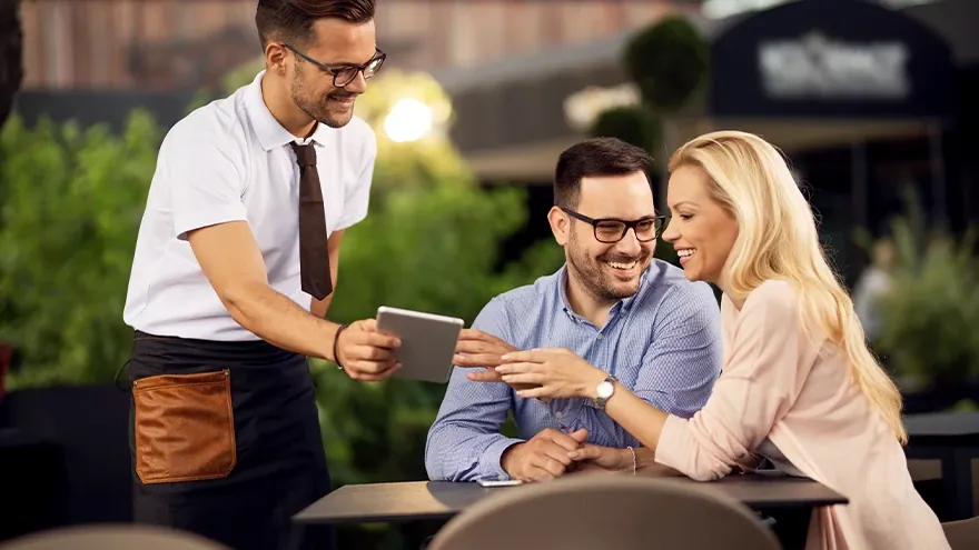 Ein Paar lässt sich auf einer Restaurantterrasse vom Kellner am Tablet beraten