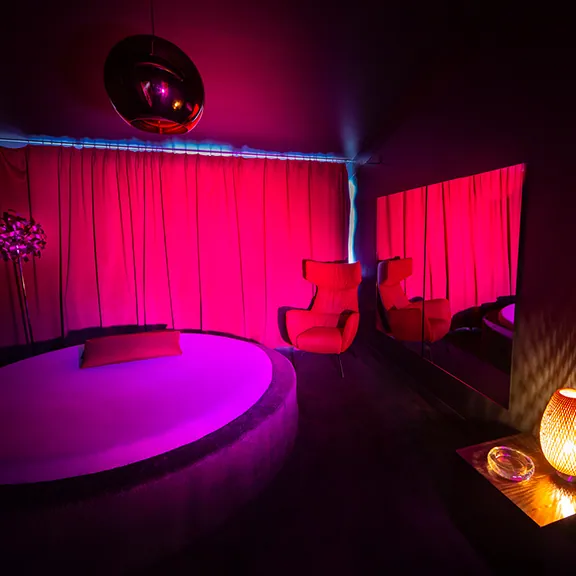 Raum im Sakura FKK Club mit pinkfarbenem Licht, rundem Podest und roten Sesseln