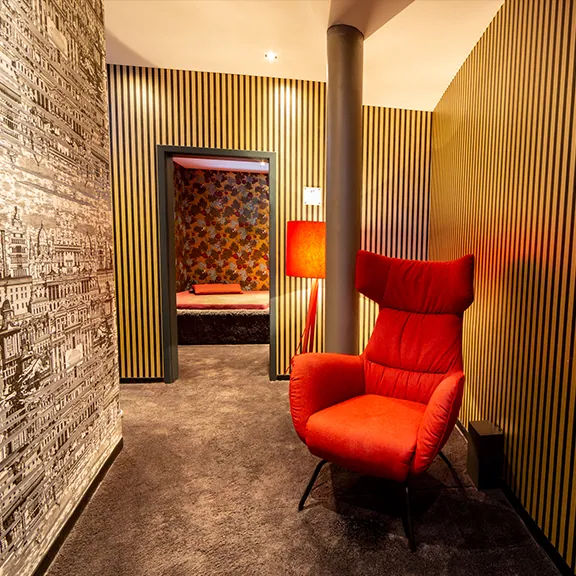 Flur einer Suite im Sakura FKK Club mit rotem Sessel, Stehlampe und gestreifter Holzwand