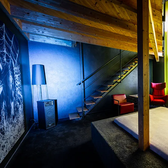 VIP-Raum im Sakura FKK Club in blauem Licht mit Holztreppe, Stehlampe und rotem Sessel