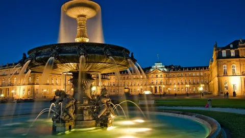 Beleuchteter Springbrunnen vor einem Barockschloss in Stuttgart bei Nacht