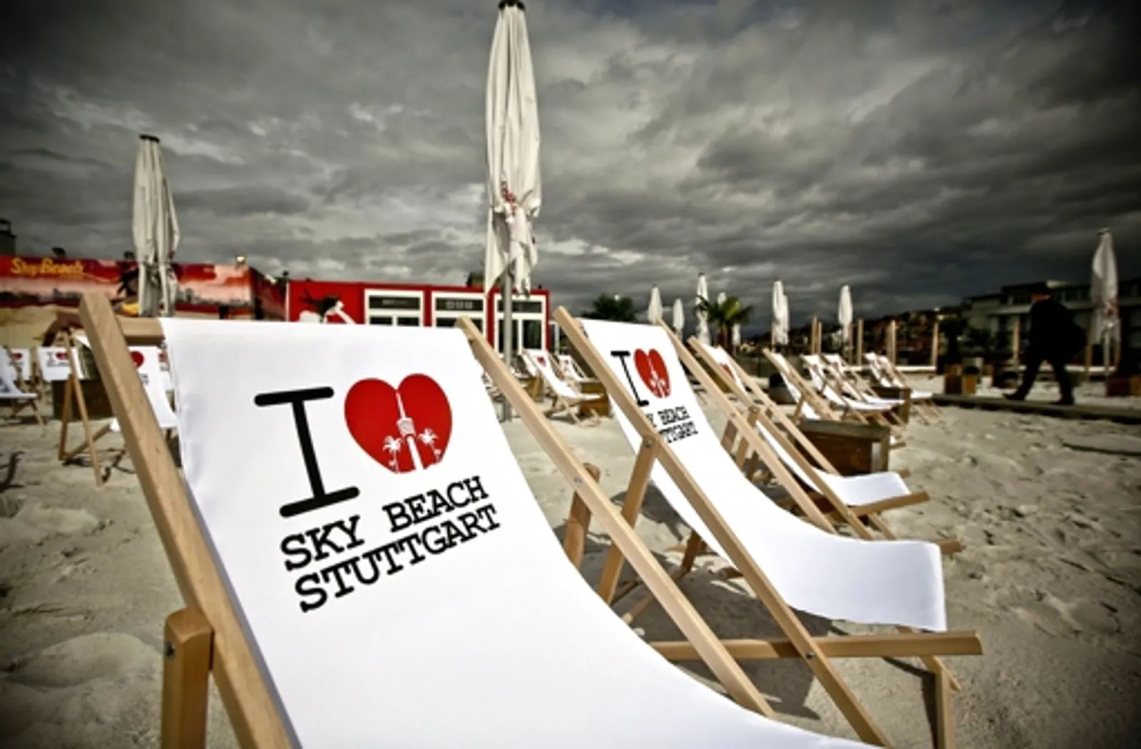 Liegestühle mit Herz-Logo und Schriftzug „Sky Beach Stuttgart“ im Sand unter grauem Himmel