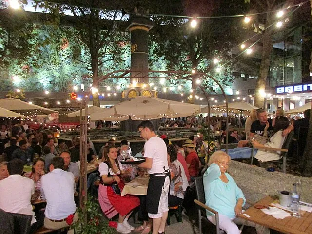 Feiernde Menschen an Tischen unter Lichterketten im Stuttgarter Weindorf am Abend