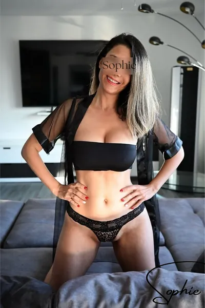 Sophie lächelnd in schwarzem Top und Spitzenslip auf einem Sofa